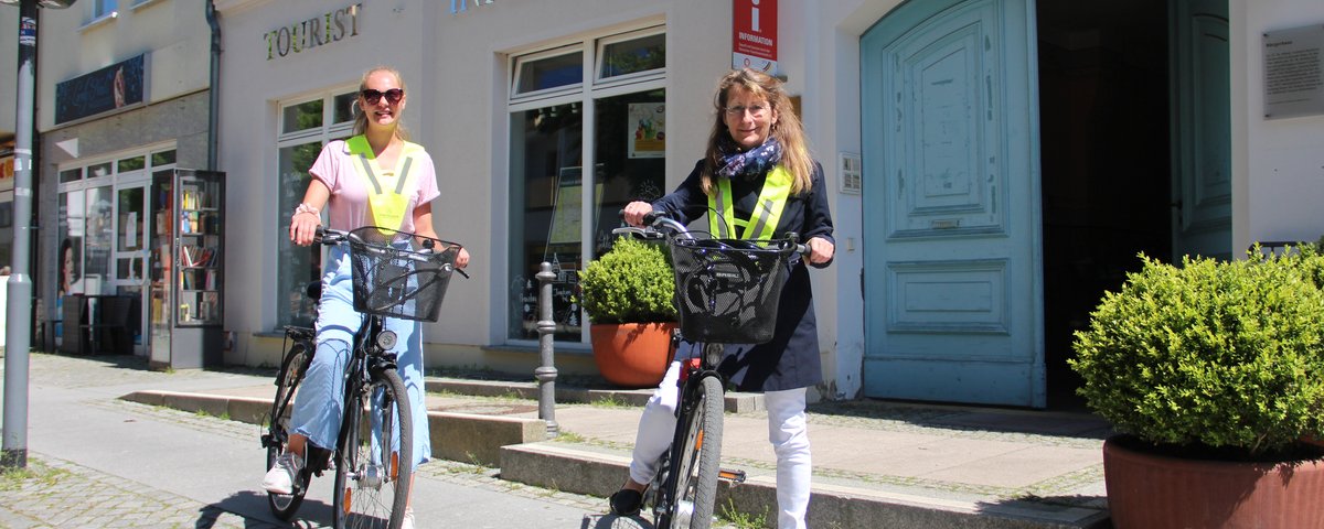 zwei Frauen auf Fahrrädern vor der Tourist-Information